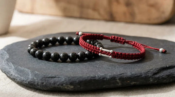 Black Tourmaline stone bracelet side by side with a braided red string protection bracelet on slate.