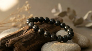 Handcrafted natural black tourmaline bead bracelet resting on dark driftwood in morning sunlight.
